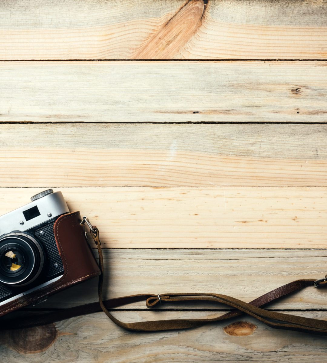 Old vintage film photo camera with brown leather strap on grunge wooden table. Photographe concept background